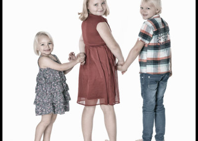 Børnefoto tre søskende holder i hånd og kigger bagud