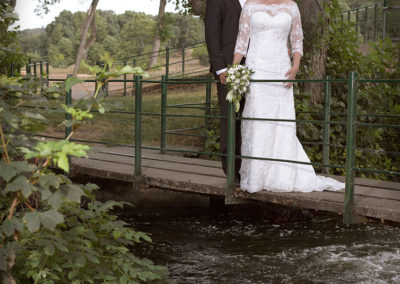 Bryllups foto med brudepar på bro gennem naturlige omgivelser.
